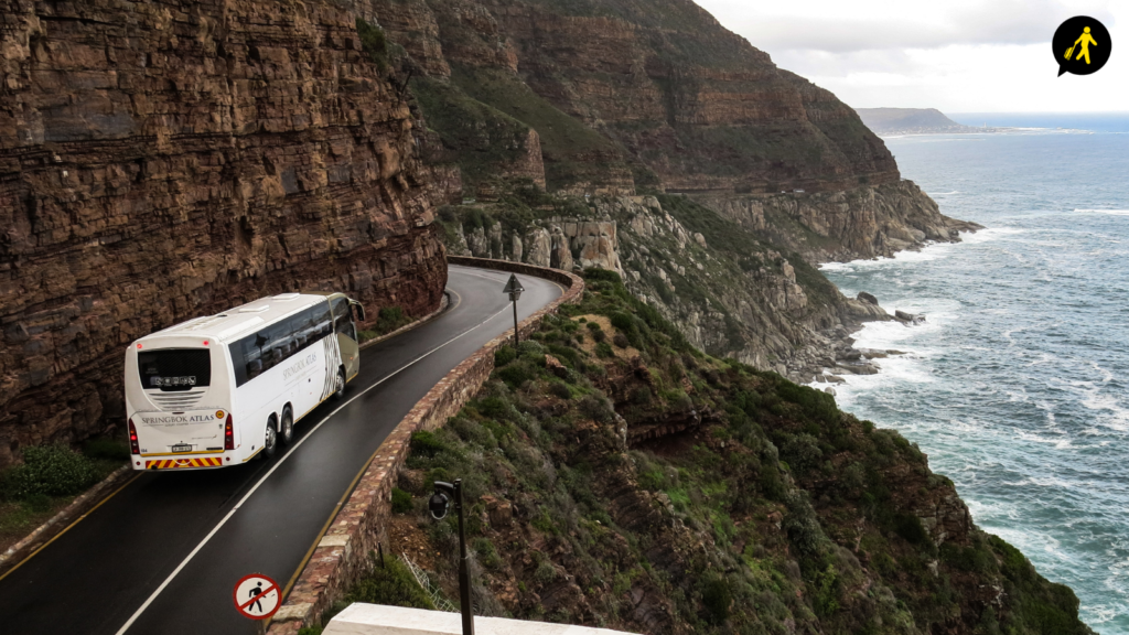 A hired coach driving on the road on a cliffside. The coach and cliff are on the left of the image, with the sea on the right.