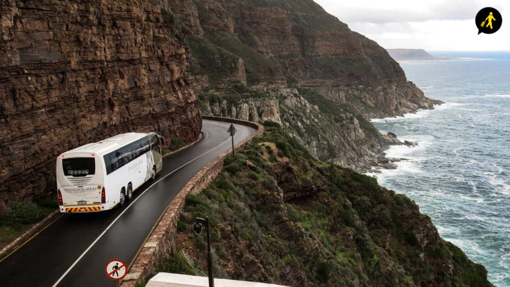 A hired coach driving on the road on a cliffside. The coach and cliff are on the left of the image, with the sea on the right. 